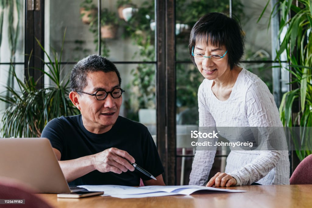 Mature man and senior woman looking at home finances with laptop Chinese couple at home with paperwork, reading documents, financial planning, organisation Couple - Relationship Stock Photo