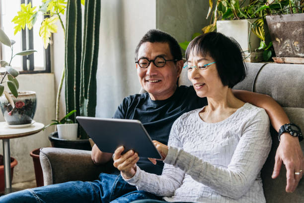 istock Cheerful Chinese couple on sofa with digital tablet 1125619203