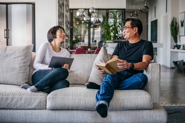istock Cheerful couple relaxing on sofa with book and electronic device 1125619277