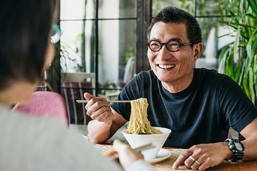 Man in his 50s talking to woman and smiling, freshly made Chinese food, noodle soup, lunch, relaxation