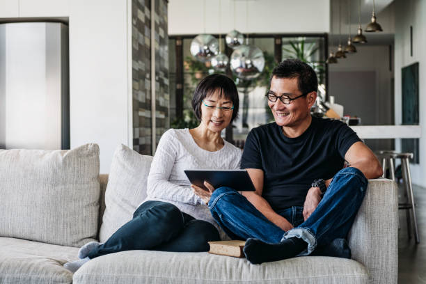 Chinese couple on sofa watching movie online Senior woman and mature man using digital tablet at home in living room, talking online, facetime, social media chinese ethnicity stock pictures, royalty-free photos & images