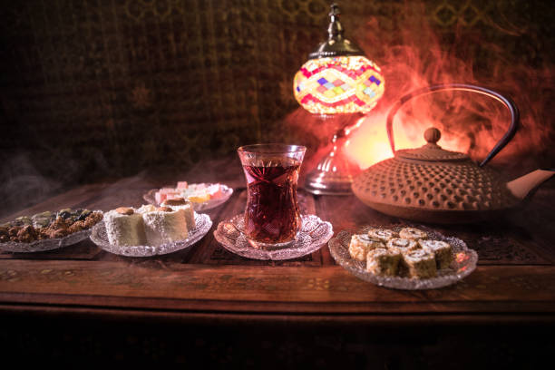 istock Arabian tea in glass with eastern snacks on vintage wooden surface. Eastern tea concept. Low light lounge interior with carpet. Empty space. 1125625594