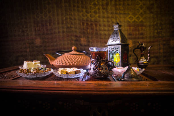 istock Arabian tea in glass with eastern snacks on vintage wooden surface. Eastern tea concept. Low light lounge interior with carpet. Empty space. 1125625620