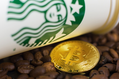 Cryptocurrency Bitcoin coin on coffee beans with Starbucks cup. Slovenia - December 01, 2018