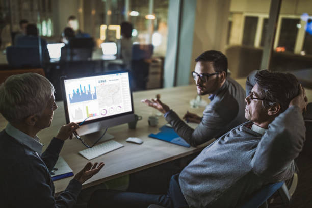 istock Business colleagues talking about charts while working on desktop PC at dark office. 1125626646