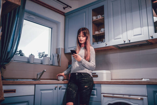 istock Adorable Girl Typing On a Smartphone From The Kitchen 1125627372