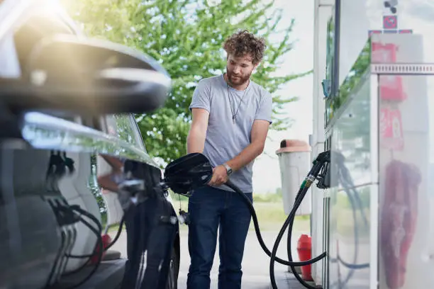 Cropped shot of a handsome young man refuelling his car at a gas station