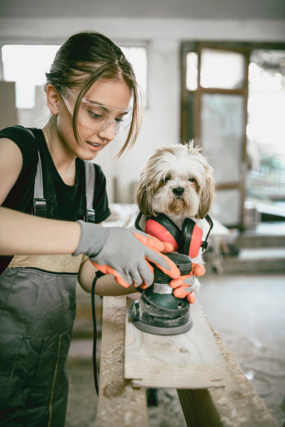 istock Female Carpenter Sanding Planks While Dog Inspector Watches 1125630575