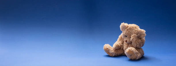 istock Teddy bear sad, holding his head, sitting in blue empty room background, banner 1125633881