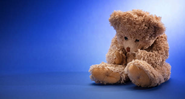 istock Teddy bear sad, holding his head, sitting in blue empty room background, copy space 1125633882