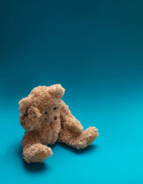 istock Teddy bear sad, holding his head, sitting in blue empty room background, copy space 1125633890
