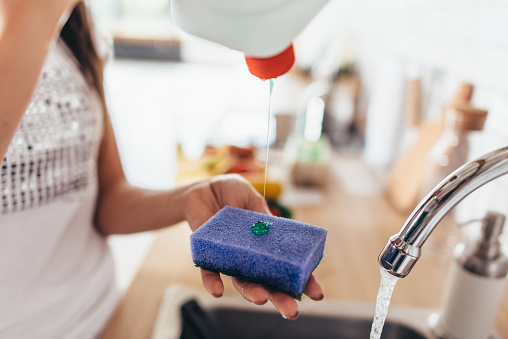 Mujer poner limpiador a una esponja para lavar la bandeja en el fregadero de la cocina. Platos de lavado de mano. Close-up. photo
