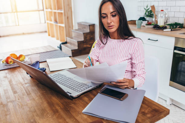 Woman working with documents and laptop in the kitchen at home
