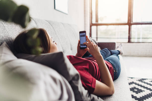 istock Young woman using smart phone while lying on the couch at home 1125637006