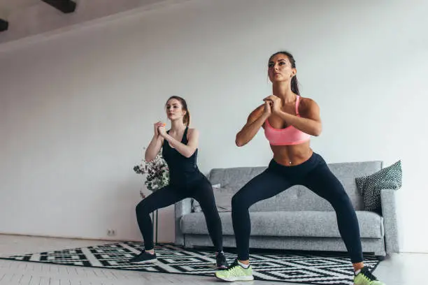 Two fit women exercising together doing squats at home.