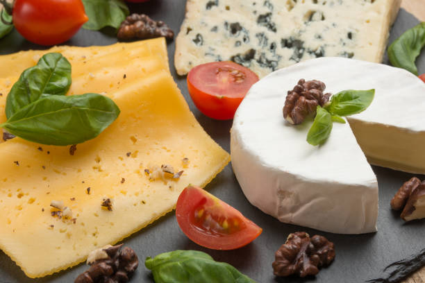 istock Different kinds of cheeses on a black board, with cherry tomatoes and basil and nuts. 1125645027