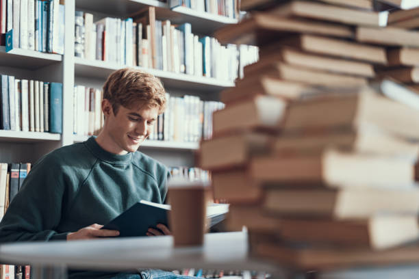 istock Calm young man sitting at the table and reading interesting book 1125648695