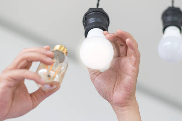 istock Power saving concept. Asia man changing compact-fluorescent (CFL) bulbs with new LED light bulb. 1125649767