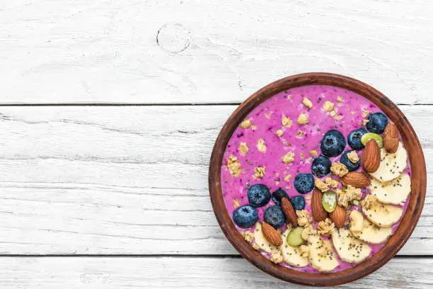Healthy vegan breakfast. acai smoothie bowl with blueberry, fruits, granola, almonds, pumpkin and chia seeds on white wooden table. detox food concept. top view