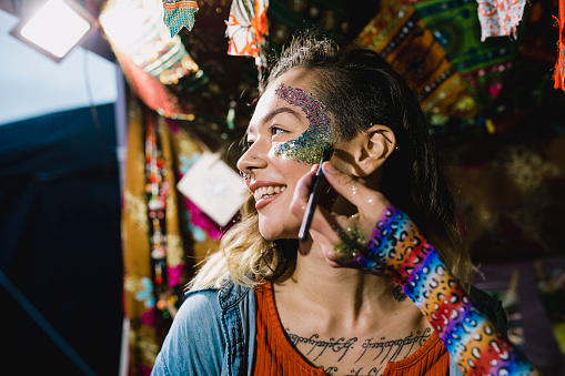 Young woman is getting glitter makeup put on her face in a tent at a music festival.
