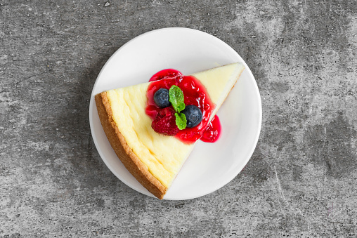 slice of cheesecake with fresh raspberries, blueberries, jam and mint on concrete background. top view. tasty breakfast