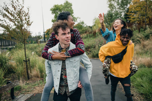 Couples Piggybacking in the Park Two young men are racing through the park with their girlfriends on their backs. teen romance stock pictures, royalty-free photos & images