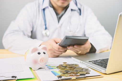 money in hospital finance relationships concept ,Doctor with piggy bank wanting payment Savings Pay Bill,Stethoscope financial checkup or saving medical insurance costs with a calculator,hight risk