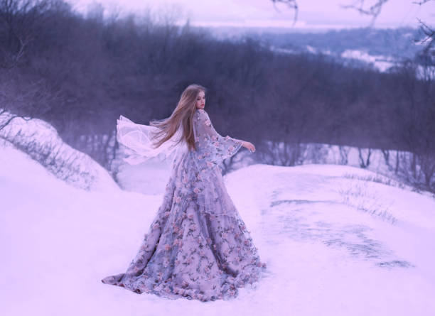 jovem com cabelo reto justo na luz voando flutuando pelo vento, vestido longo roxo lilás decorado com flores destaca-se em uma colina no inverno na neve na floresta. foto de arte. cores frias - straight hair fashion model women long hair - fotografias e filmes do acervo