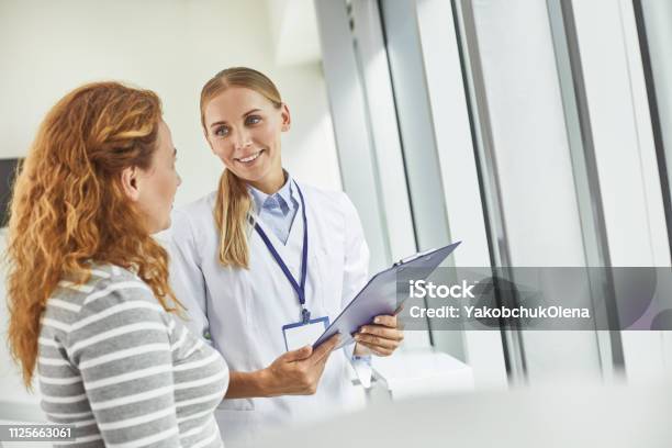 Giovane Medico In Possesso Di Appunti Mentre Guarda Il Paziente - Fotografie stock e altre immagini di Medico