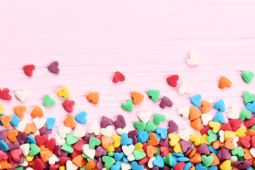Colorful heart shaped sprinkles on pink wooden table