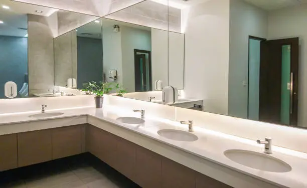Faucets with washbasin and big mirror in public restroom