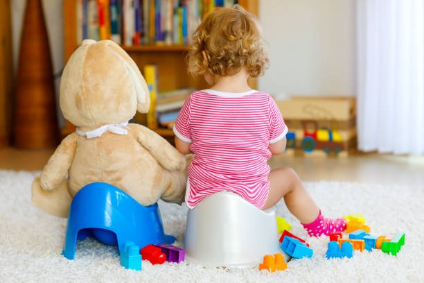 Closeup of cute little 12 months old toddler baby girl child sitting on potty. Kid playing with big plush soft toy. Toilet training concept. Baby learning, development steps Closeup of cute little 12 months old toddler baby girl child sitting on potty. Kid playing with big plush soft toy. Toilet training concept. Baby learning, development steps. potty toilet child bathroom stock pictures, royalty-free photos & images