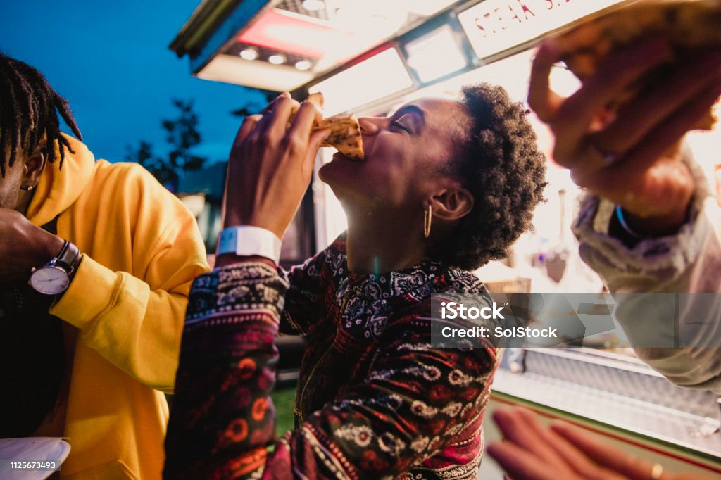 Young Woman Eating Pizza at Festival A young women enjoying pizza with friends at a music festival. Eating Stock Photo