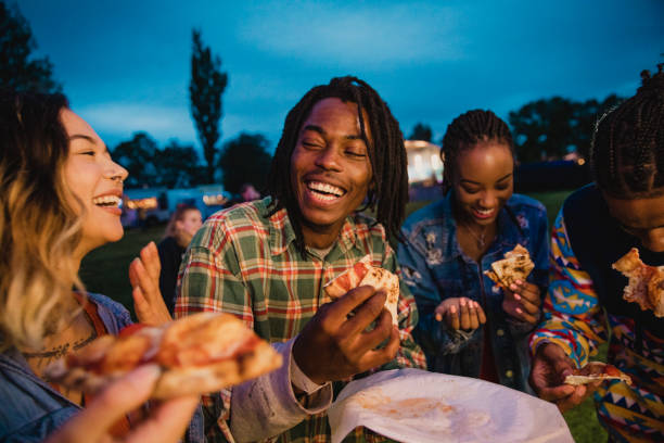 Pizza Festival Fun A young group of friends laughing and sharing pizza at a music festival. food festival stock pictures, royalty-free photos & images