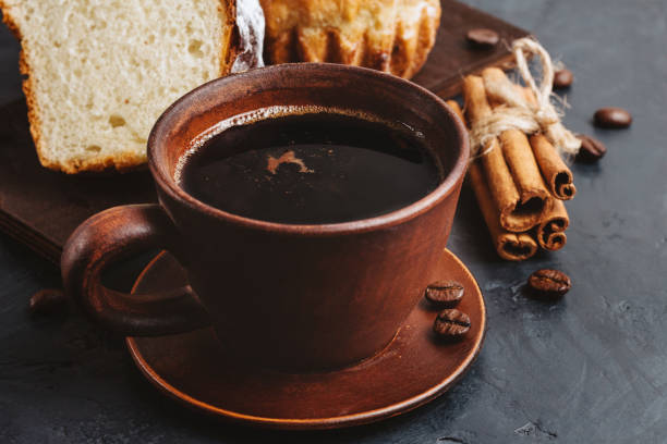 istock Cup with hot coffee, muffins and cinnamon sticks on the dark, textured background 1125680088