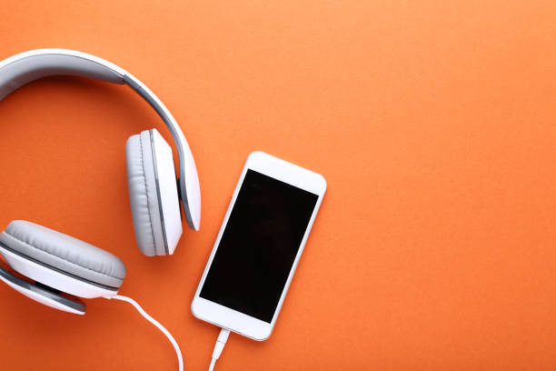 smartphone con auriculares en fondo naranja - orange white audio fotografías e imágenes de stock