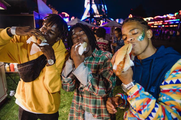 Hot Dogs Taste Better at the Funfair Three young men are indulging in to hot dogs from a van at a funfair. hot dog stand stock pictures, royalty-free photos & images