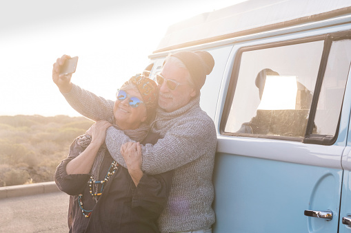 Happy old senior adult couple enjoy and have fun together with love in vacation and outdoor leisure activity using modern smart ph0ne to take picture selfie hugging and smiling with sun in backlight