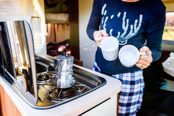 Cooking coffee in campervan, caravan or RV on camping trip. Cooking coffee in campervan, caravan or RV on camping trip. Woman is making coffee in the morning using italian kafetiera on a family vacation camping trip. family-van-driving stock pictures, royalty-free photos & images