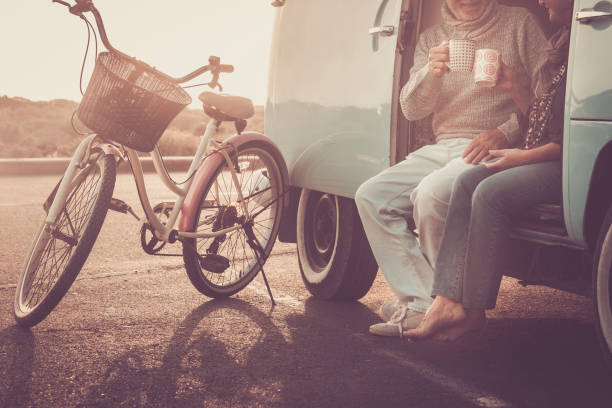not recognizable couple of caucasian couple having fun and drinking coffee together sitting outside the old vintage van with bike parked outdoor - sunset time and vacation alternative travel concept not recognizable couple of caucasian couple having fun and drinking coffee together sitting outside the old vintage van with bike parked outdoor - sunset time and vacation alternative travel concept hippie photos stock pictures, royalty-free photos & images