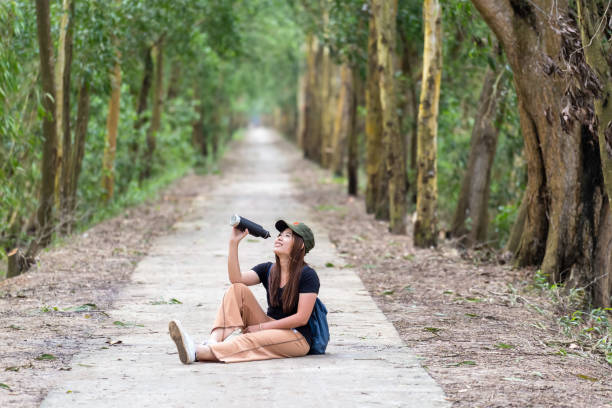 mulher asiática em traje casual, beber a água da garrafa de esporte com relaxar ação na floresta profunda no conceito de tempo, estilo de vida e lazer da noite - running jogging women marathon - fotografias e filmes do acervo