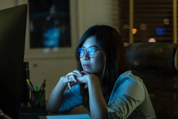 Photo of Portrait of Asian Businesswoman working hard and looking the digital graphic on the table with front of computer desktop in workplace at late with serious action, Work hard and too late concept