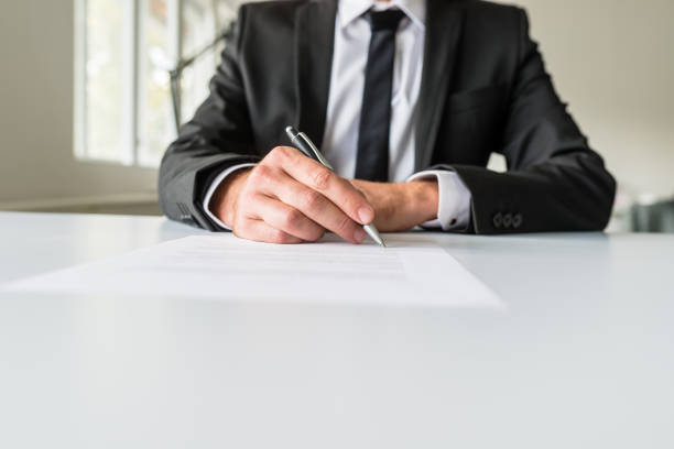Front view of businessman or employer sitting at his office desk signing a contract or employment paper with a pen.