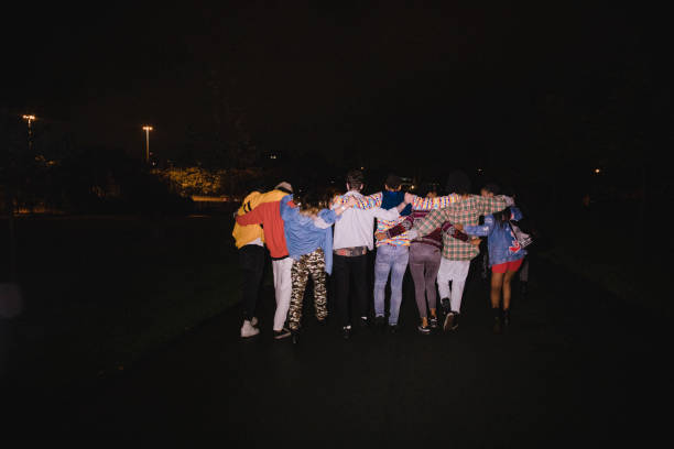 Children of the Night Rear view shot of eight young adults walking down a street at night with their arms round each other. alternative pose photos stock pictures, royalty-free photos & images