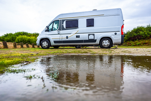 Campervan or motorhome camping on rainy day with rain puddles. Family vacation road trip with camper van, motor home or RV in with bad weather. Holiday travelling to Atlantic ocean - Spain or Portugal