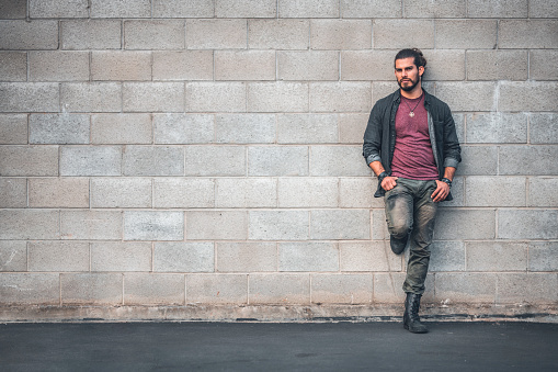 Portrait of confident male hipster. Smiling man is wearing casuals. He is leaning against wall at city.