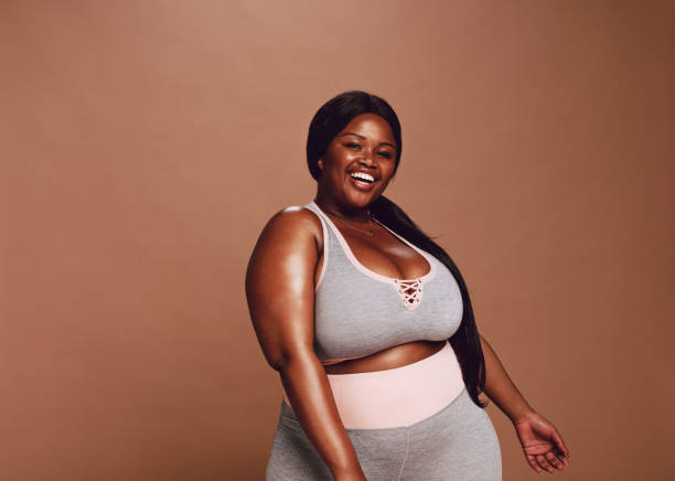 Oversize sporty african woman Large african woman looking happy on brown background. Plus size female in sports clothing looking at camera and laughing. body confidence stock pictures, royalty-free photos & images