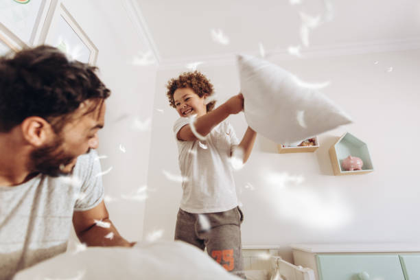 niño jugando con su padre en la casa con cojines - lucha con almohada fotografías e imágenes de stock