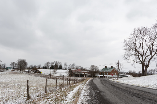 Winter landscape in rural Appalachia. A road leads to an old barn and farmhouse with a pasture to the left and negative space above for copy.