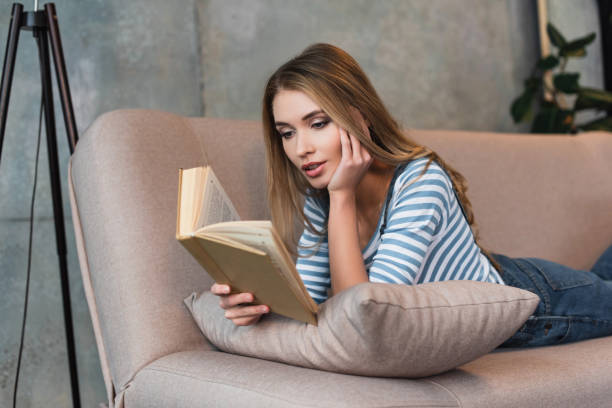 istock selective focus of young beautiful woman reading book and lying on sofa 1125698267